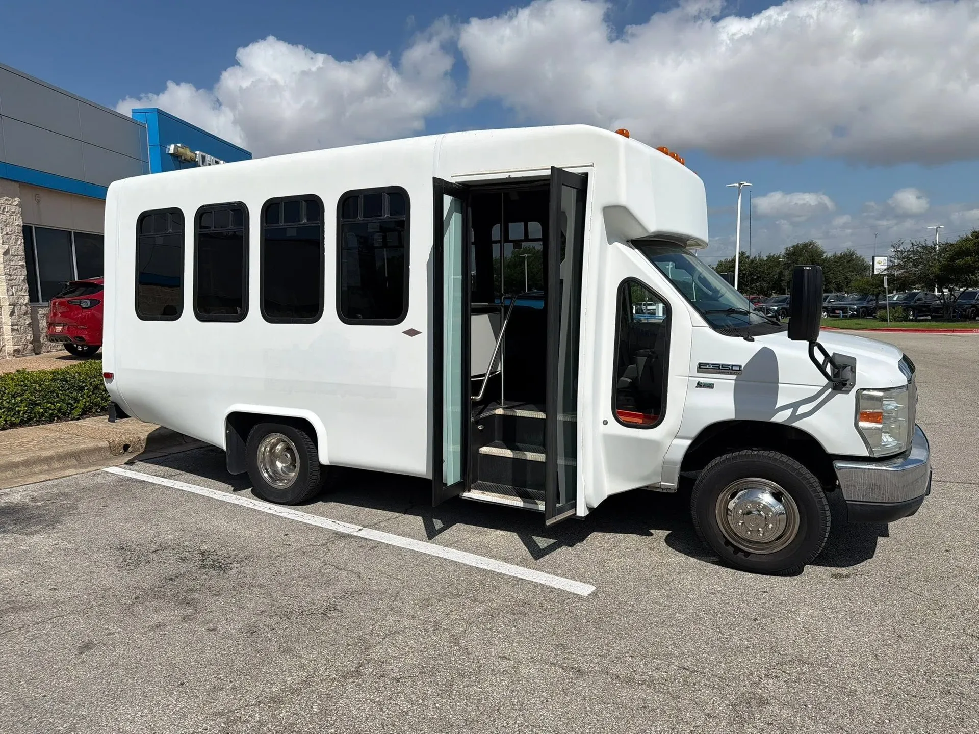 Real 2013 Ford E-350 14-passenger minibus with the passenger door open in a sunlit commercial lot